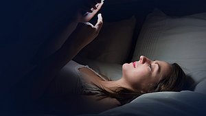 Frau mit Handy liegt im Bett